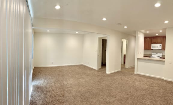 an empty living room with a kitchen in the background