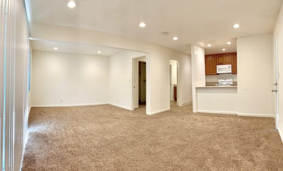 an empty living room with a kitchen in the background
