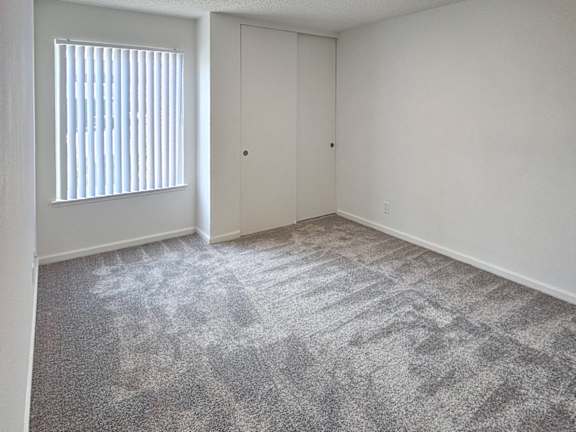A room with a carpeted floor and a window with blinds.