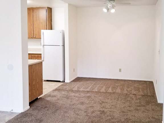 A white refrigerator is in a kitchen with brown carpeting.