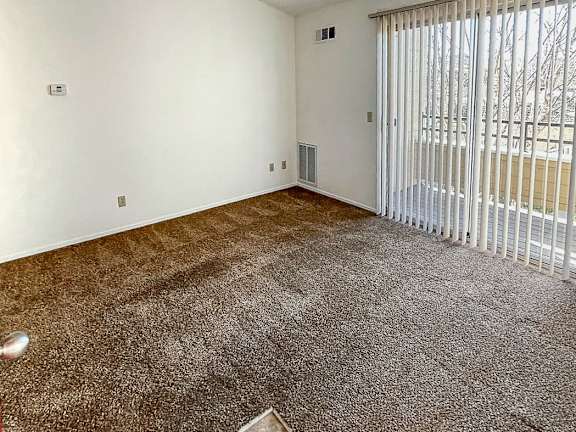 A room with a carpeted floor and a window with blinds.
