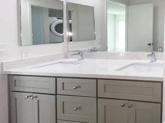 A bathroom with a white sink and grey cabinets.