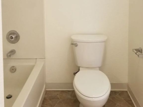 A white toilet in a bathroom with a white tub.