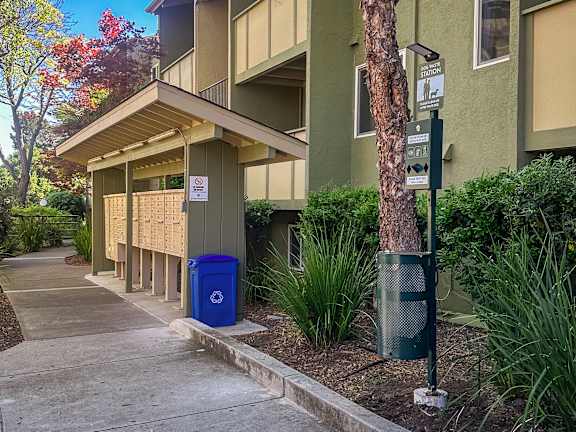 A blue recycling bin sits on a sidewalk in front of a green building.