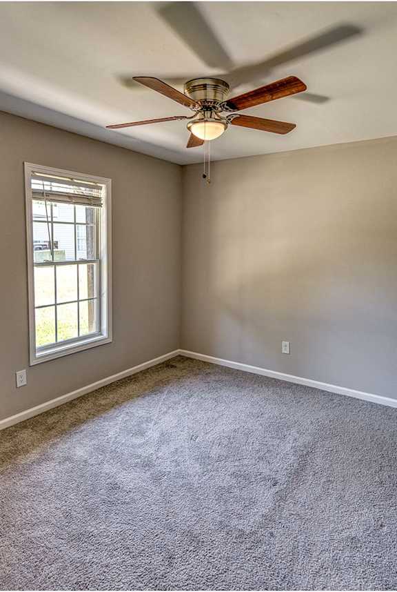 an empty living room with a ceiling fan and a window