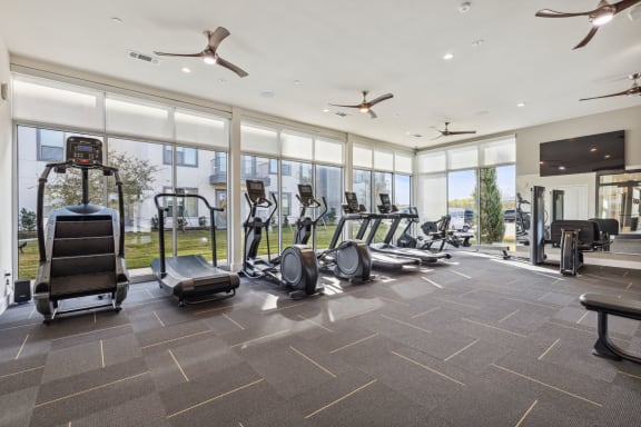 the state of the art gym is equipped with cardio equipment and floor to ceiling windows at LynnCora in Grand Prairie, TX
