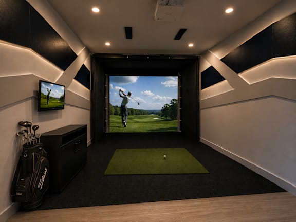 A room with a golf mat and a TV showing a golfer.
