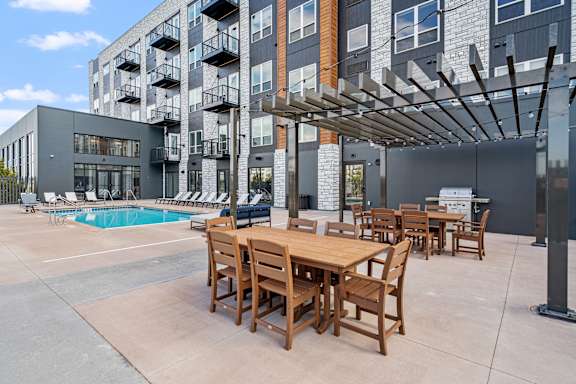 A wooden table and chairs are set up outside a building with a pool.
