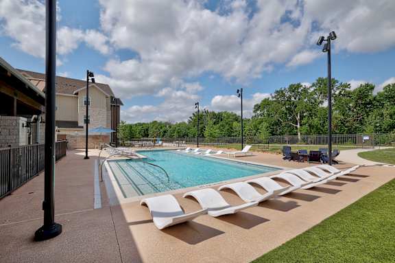A large outdoor swimming pool with sun loungers and a building in the background.