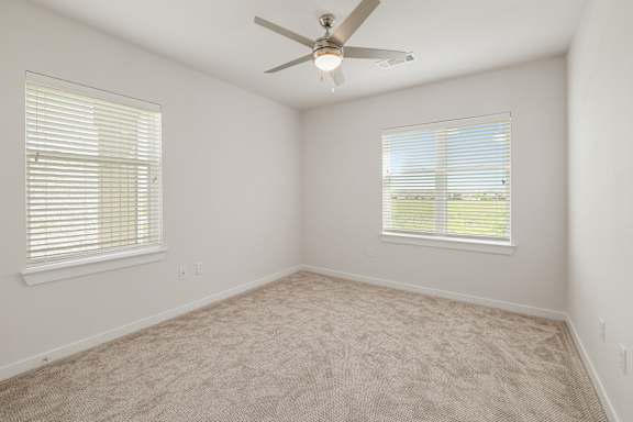A room with a ceiling fan and two windows.