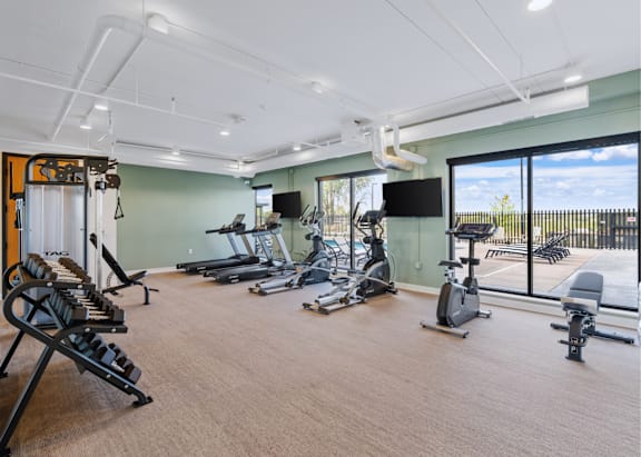 a spacious fitness room with cardio equipment and a large window with a view of the pool