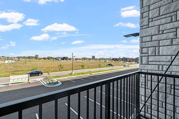 A balcony overlooks a parking lot and a road with a car and a signboard.
