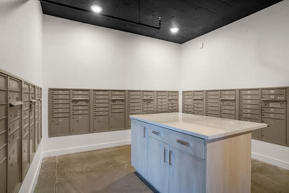 A room with a white counter and brown cabinets with a wall of mailboxes.