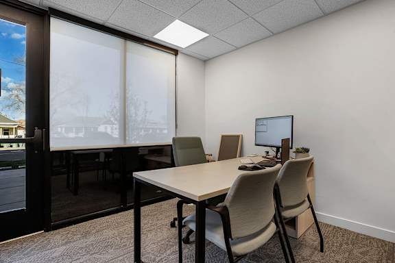 A room with a desk and chairs with a window in the background.