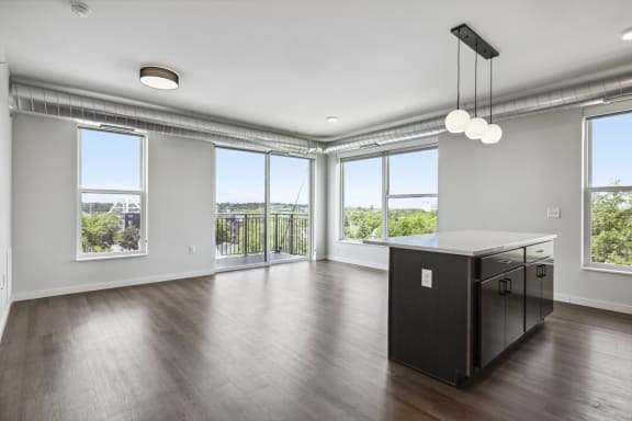 an empty living room with a large window and a kitchen