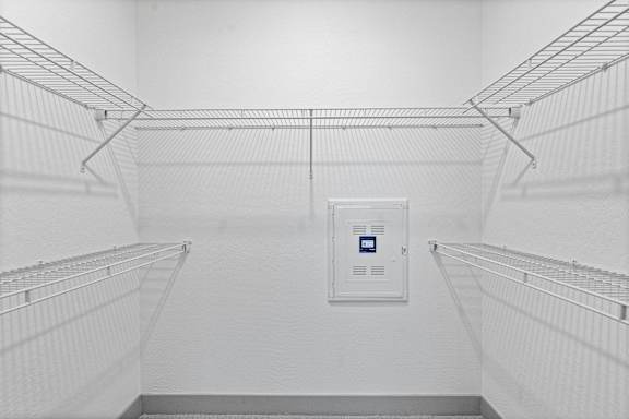 A white refrigerator with a blue label on the door is in the center of a room with wire shelves on the walls.