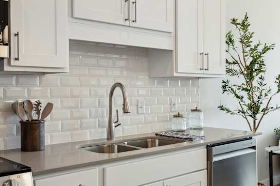 A kitchen with a white tile backsplash and white cabinets.