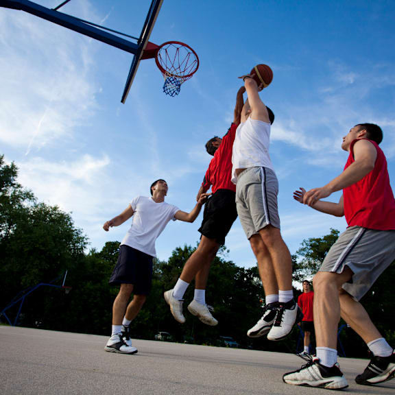 Four men playing basketball on a sunny day. at The Dean at Creekview Apartments, Newark, Delaware