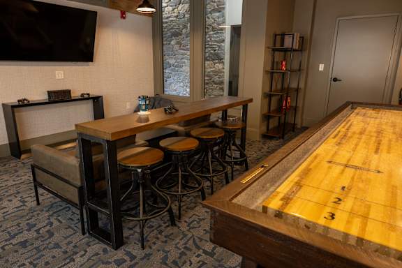 A shiny wooden pool table in the middle of a room with a bar and stools.