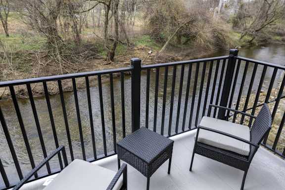 A balcony with a chair and table overlooking a river at The Dean at Creekview Apartments, Newark, Delaware