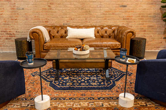 A brown leather couch with a white pillow and a coffee table with a bowl of fruit on it.