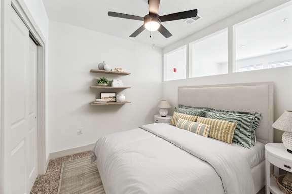 A bedroom with a bed, a ceiling fan, and a nightstand with a lamp.