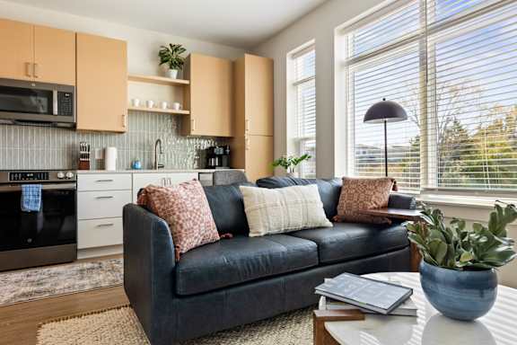 A black couch with pillows sits in a living room with a kitchen in the background at Hawkins Press Apartments, Charlotte, NC