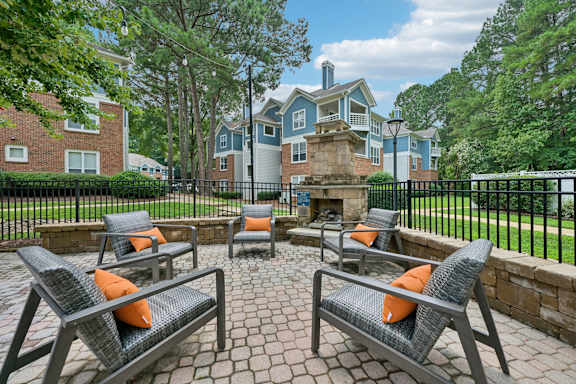 Four chairs are arranged around a fire pit on a brick patio.