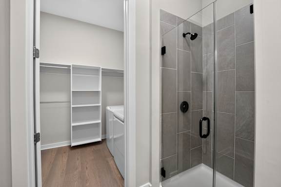 A walk-in shower with a glass door and a white cabinet with shelves.
