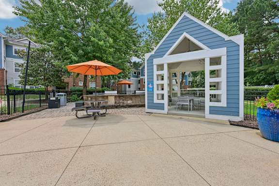 A small blue building with an orange umbrella sits in the middle of a paved area.