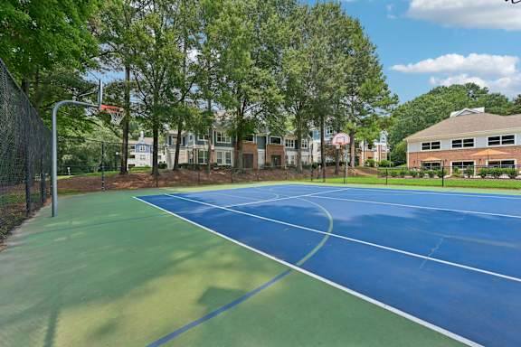 A blue and green tennis court surrounded by trees and buildings.