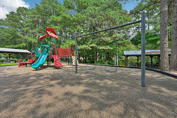 A playground with a red and green slide, a monkey bars, and a swing set.