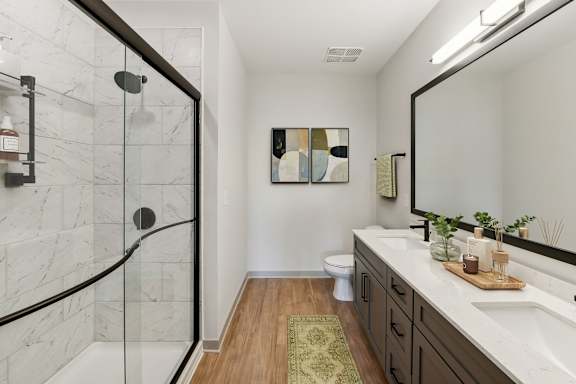 A bathroom with a marble shower and a wooden floor.