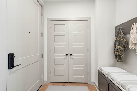 A white door is in a hallway with a bench and coat rack.