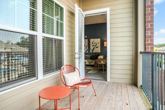A red chair and table are on a wooden deck outside a house.
