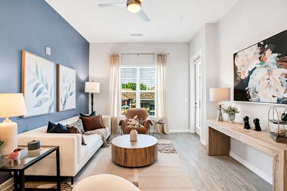 A modern living room with a white sofa, a wooden coffee table, and a large painting on the wall.