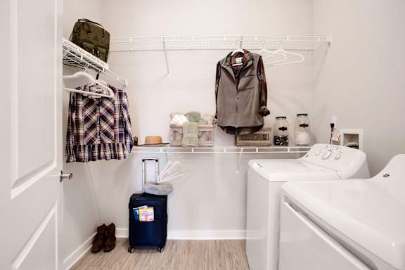 A small bathroom with a white sink, a blue suitcase, and a brown jacket hanging on the wall.