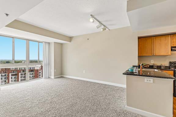 A spacious living room with a kitchenette and a view of a building outside the window.