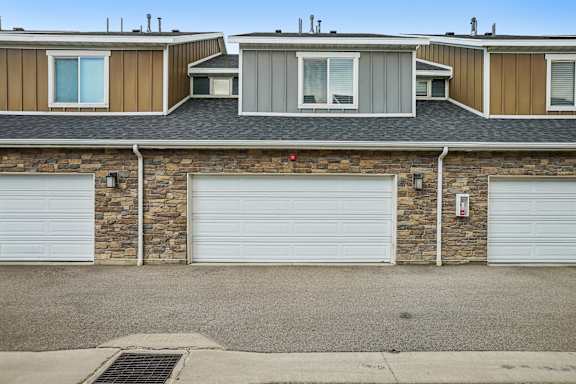 A house with a stone wall and three garage doors.