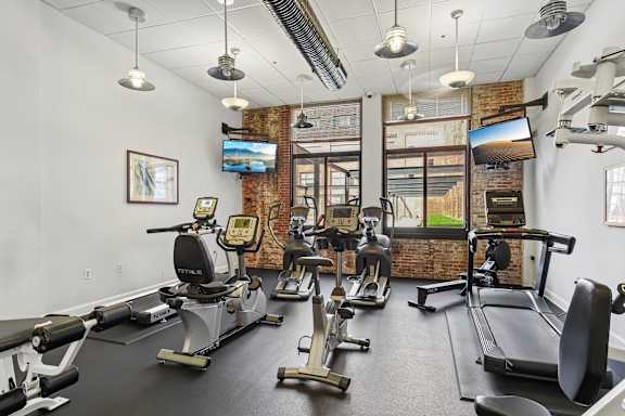 A gym with a brick wall and a row of treadmills  a room with tables and chairs and a computer in a room at Tindeco Wharf, Baltimore Maryland