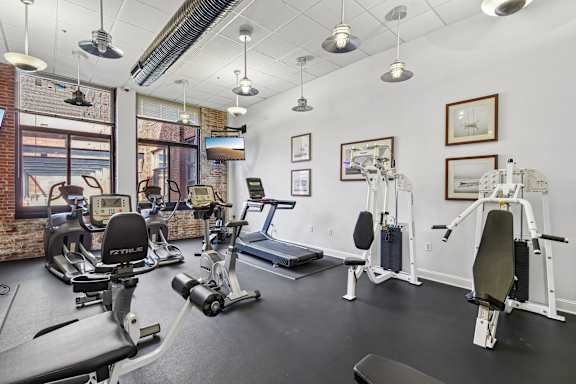 A gym with a variety of equipment including treadmills, stationary bikes, and weight machines  a room with tables and chairs and a computer in a room at Tindeco Wharf, Baltimore Maryland