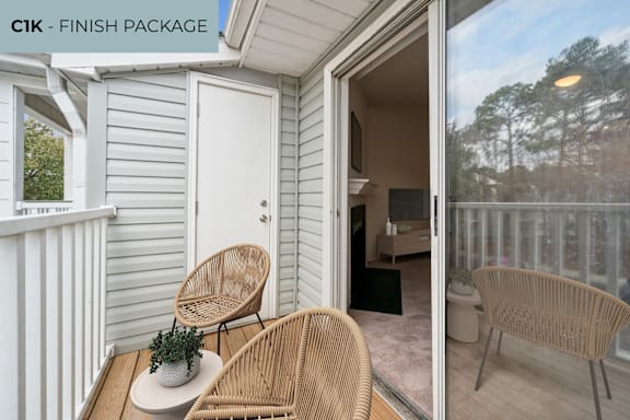 A white door is on the left of a balcony with two chairs and a table.