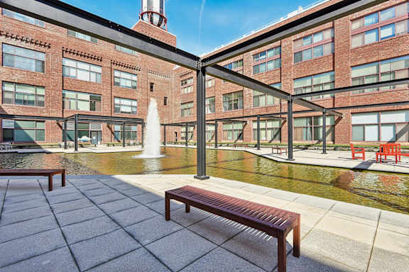 A bench is in front of a fountain in the courtyard at Tindeco, Wharf, Baltimore, MD 21224
