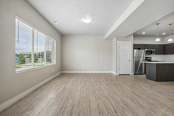 A spacious room with wooden flooring and a kitchen area in the background.