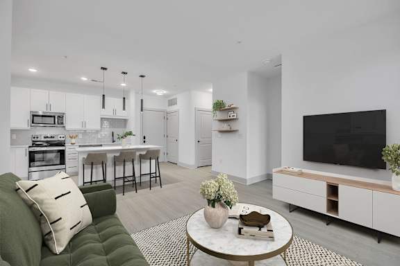 A modern living room with a green couch and a white kitchen in the background