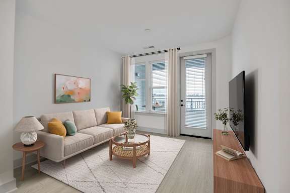 A living room with a couch, a coffee table, a lamp, a plant, a painting, and a flat screen TV