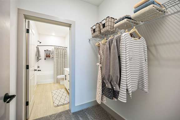 A white closet with clothes hanging and a doorway leading to a bathroom