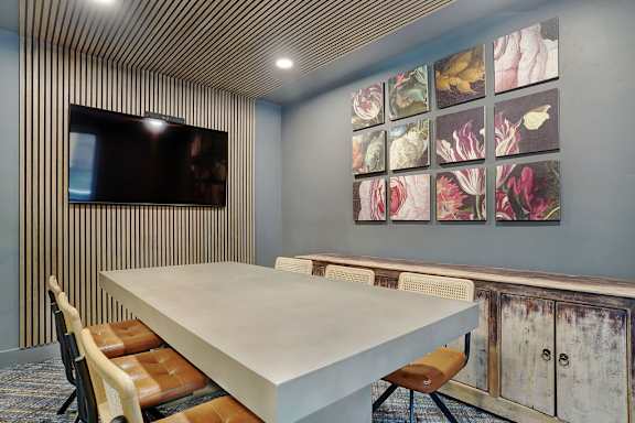 A conference room with a long table and chairs, a television, and a wall of framed pictures.