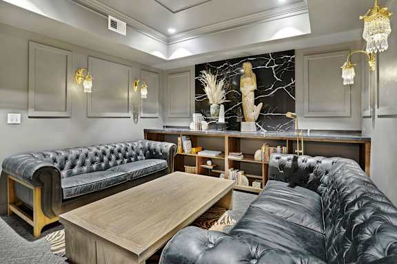 A black leather couch sits in a well-lit room with a wooden coffee table in front of it.