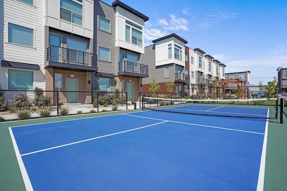 A tennis court is surrounded by apartment buildings.